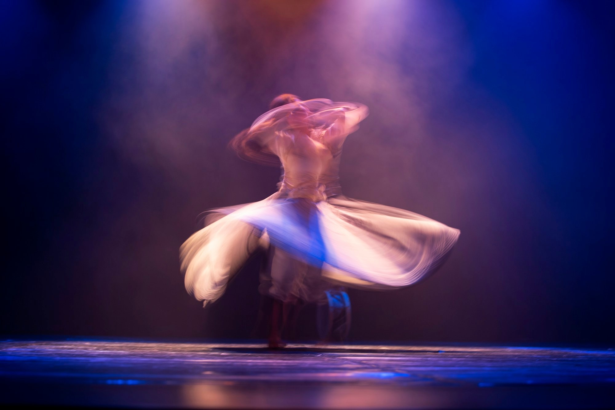 A dancer spinning mid-performance, skirt flaring under blue and warm stage light