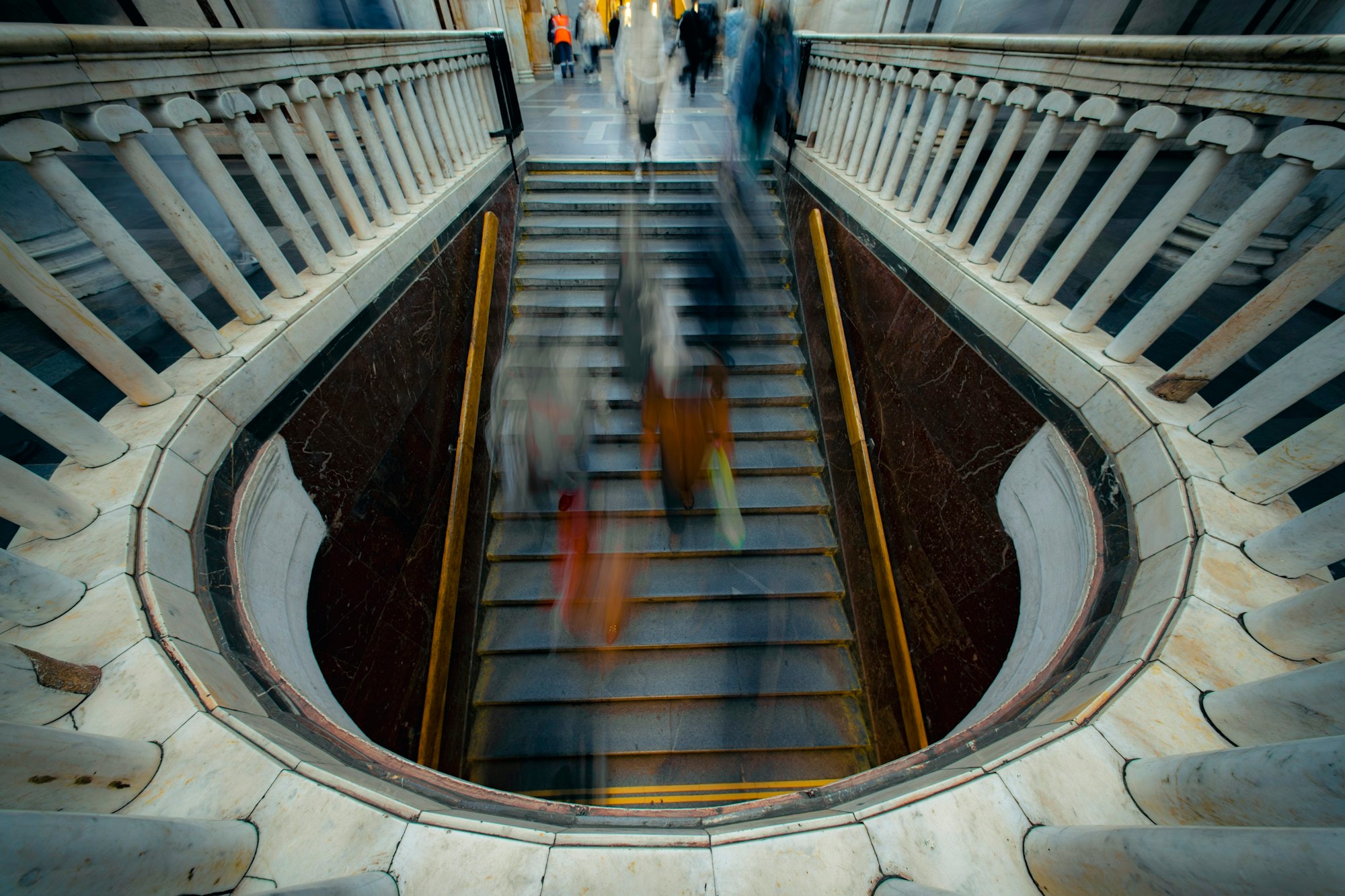 Blurred figures descending a grand marble staircase