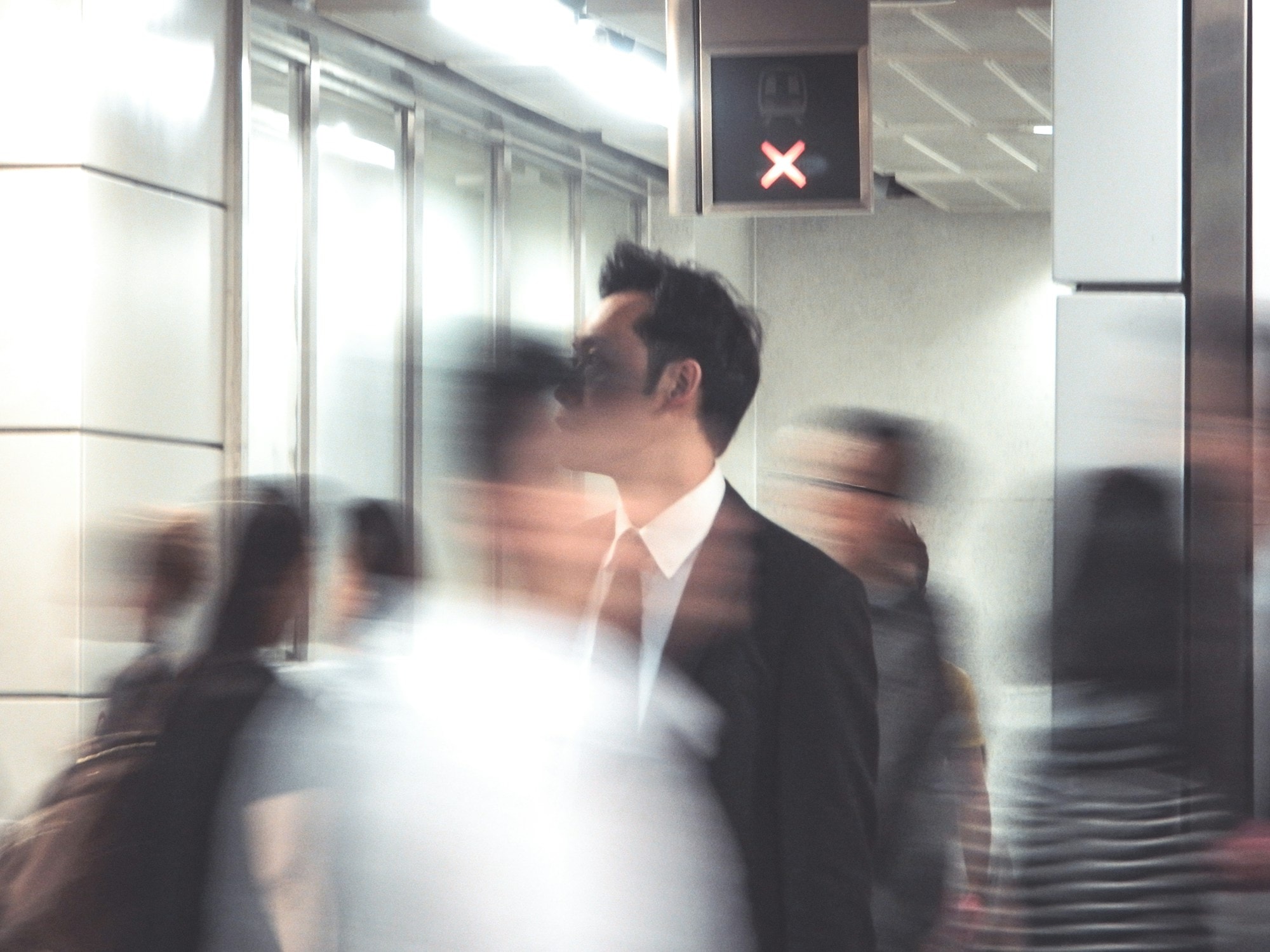 A suited commuter standing still amid a blur of people moving through a station